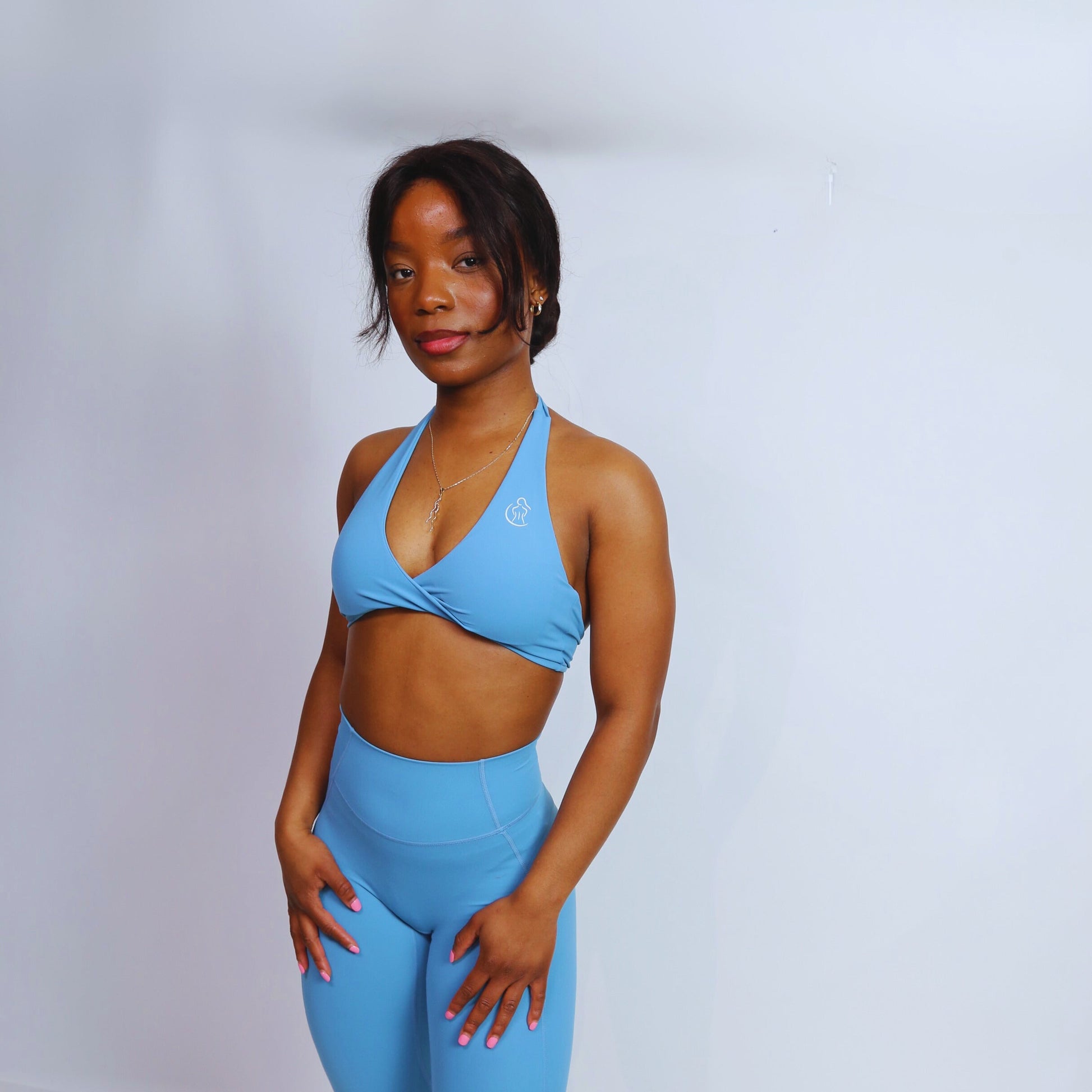 A female model wearing Spa blue halter sports bra with a twist front design, matching blue leggings.