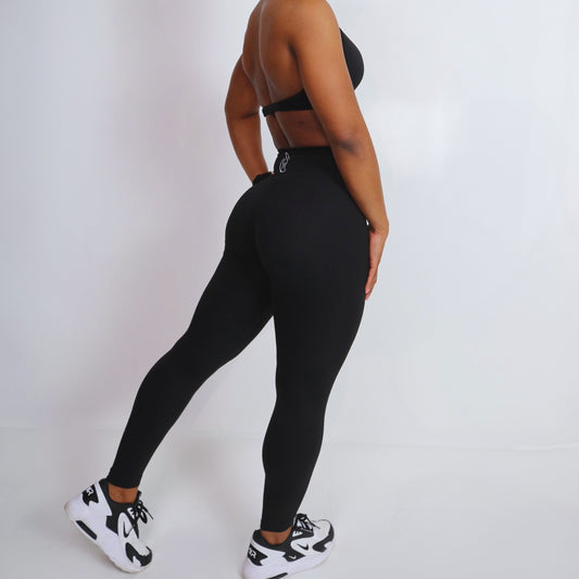 A model wearing high-waist black leggings with a cinched waist with aesthetic trim detailing.